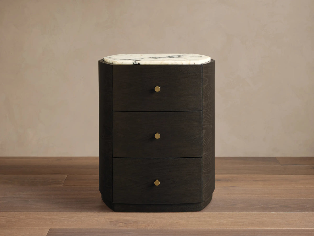 Front view of the dark brown Elton Nightstand, featuring three drawers with satin brass knobs and a white marble top with grey veining.