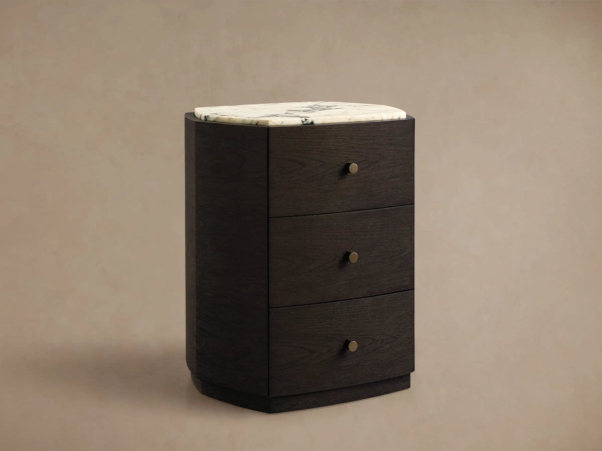 Front view of the Elton Nightstand, featuring dark wood, a white marble top, three drawers, and satin brass knobs.
