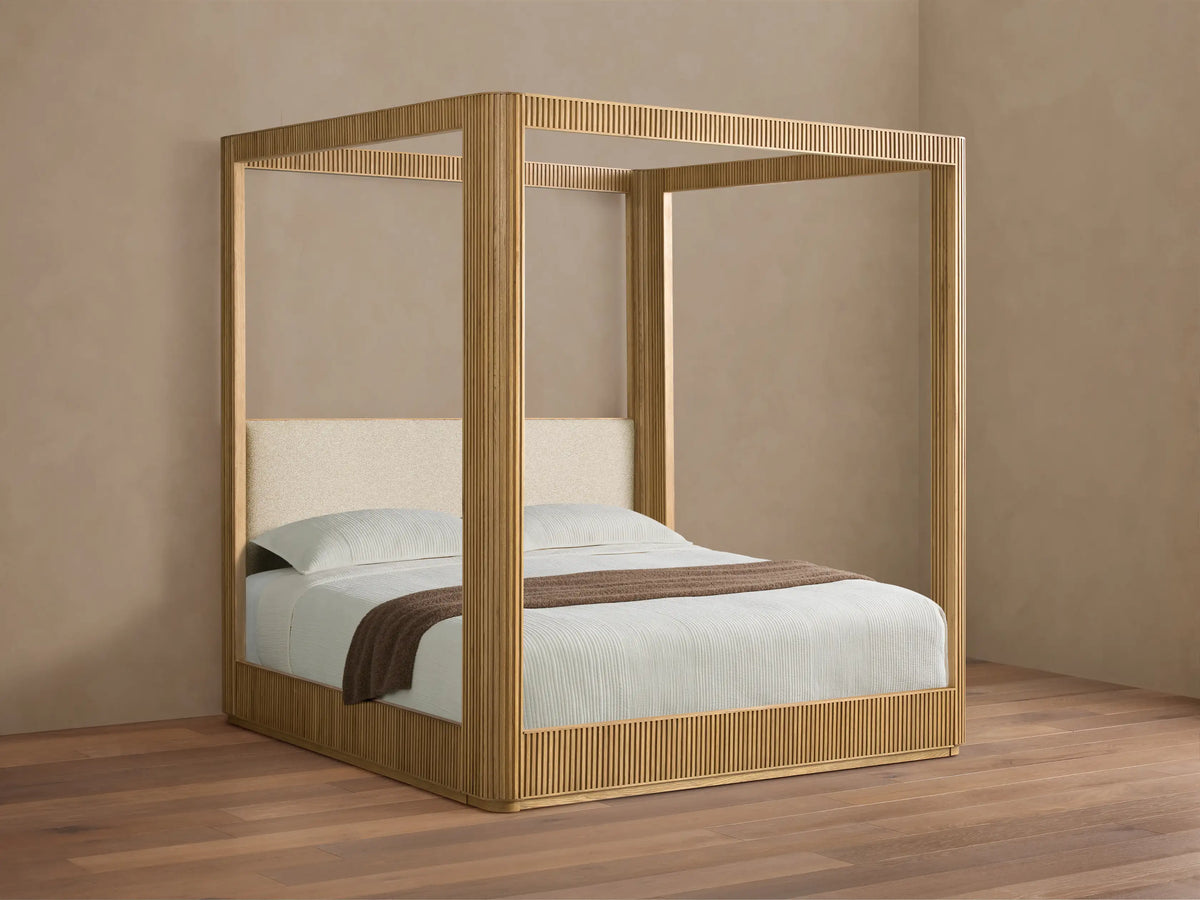 Front view of the Finnley Canopy Bed, featuring a light natural wood frame with reeded details and a cream upholstered headboard.