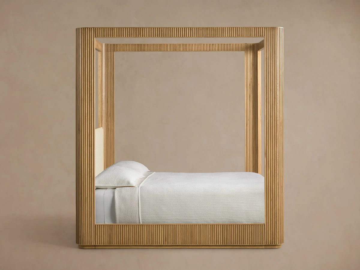 Close-up of the Finnley Canopy Bed with a light oak wooden frame, cream textured fabric, and a fluted side panel.