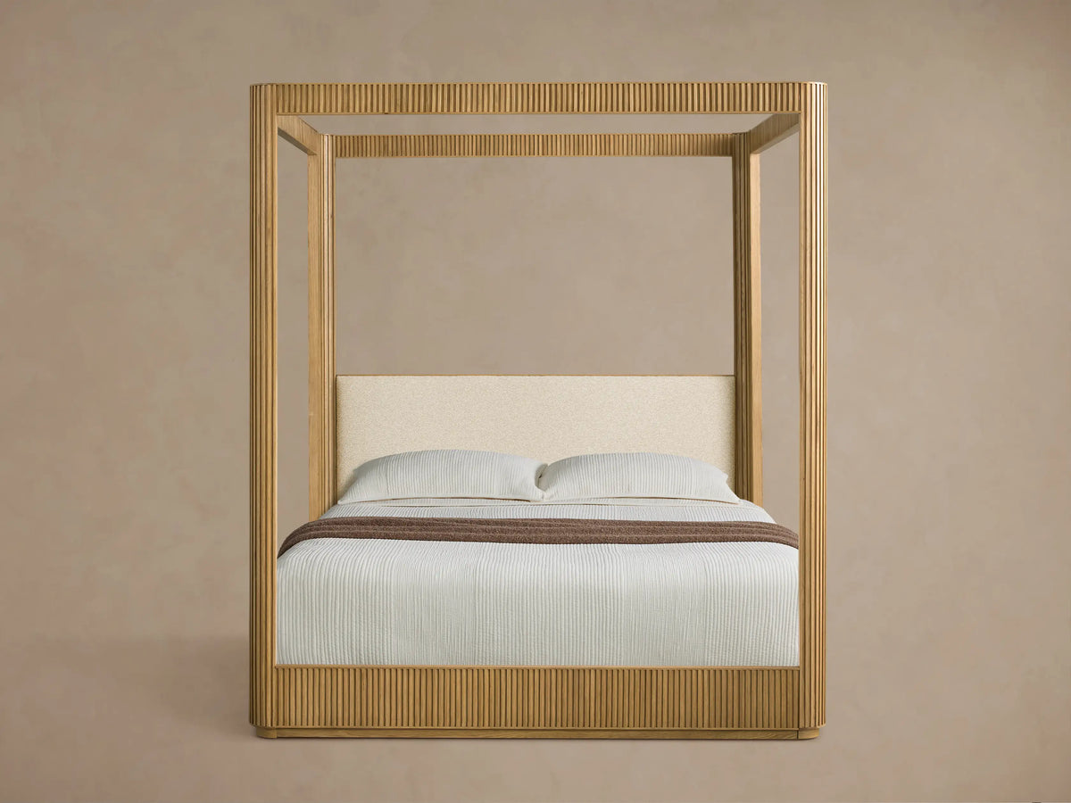 Front view of the Finnley Canopy Bed, made of light fluted wood, with white bedding and a cream upholstered headboard.