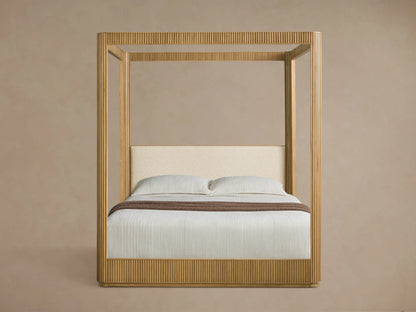 Front view of the Finnley Canopy Bed, made of light fluted wood, with white bedding and a cream upholstered headboard.
