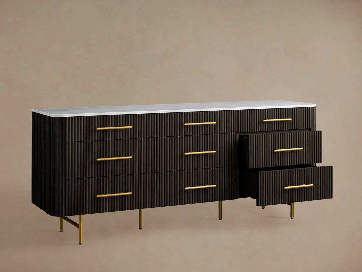Finnley Nine-Drawer Dresser in dark finish with a sleek white marble top. Features nine drawers with brass-finished handles and slim legs.