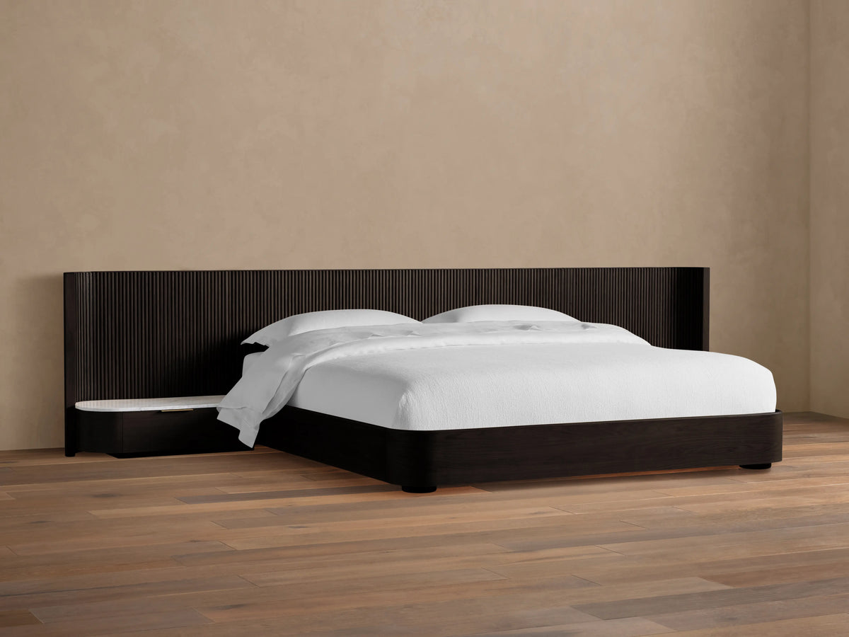 Finnley Extended Headboard Bed in dark wood finish, low-profile design, with white bedding, against a beige wall.