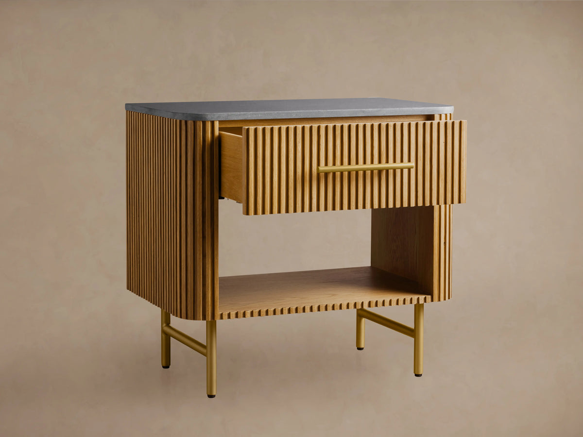 Finnley Open Nightstand: Honey wood with reeding, gray stone top, a drawer with brass pull, an open shelf, and golden legs.