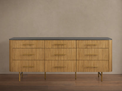 Front view of Finnley Nine-Drawer Dresser in honey-finished oak with vertical reeding, dark stone top, brass handles & legs.