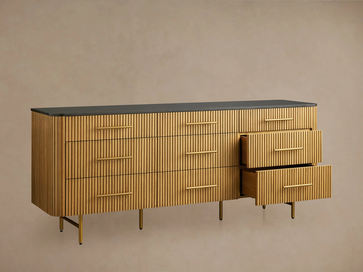 Front view of Finnley Nine-Drawer Dresser in honey-finished oak with vertical reeding, dark stone top, brass handles & legs.