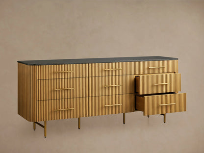 Front view of Finnley Nine-Drawer Dresser in honey-finished oak with vertical reeding, dark stone top, brass handles & legs.