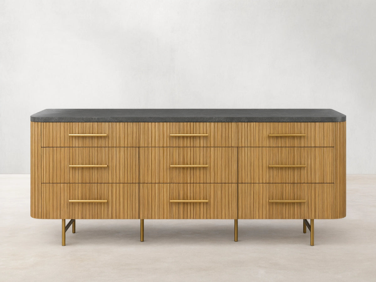 Front view of Finnley Nine-Drawer Dresser in honey-finished oak with vertical reeding, dark stone top, brass handles & legs.
