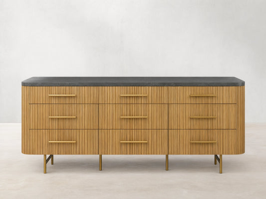 Front view of Finnley Nine-Drawer Dresser in honey-finished oak with vertical reeding, dark stone top, brass handles & legs.