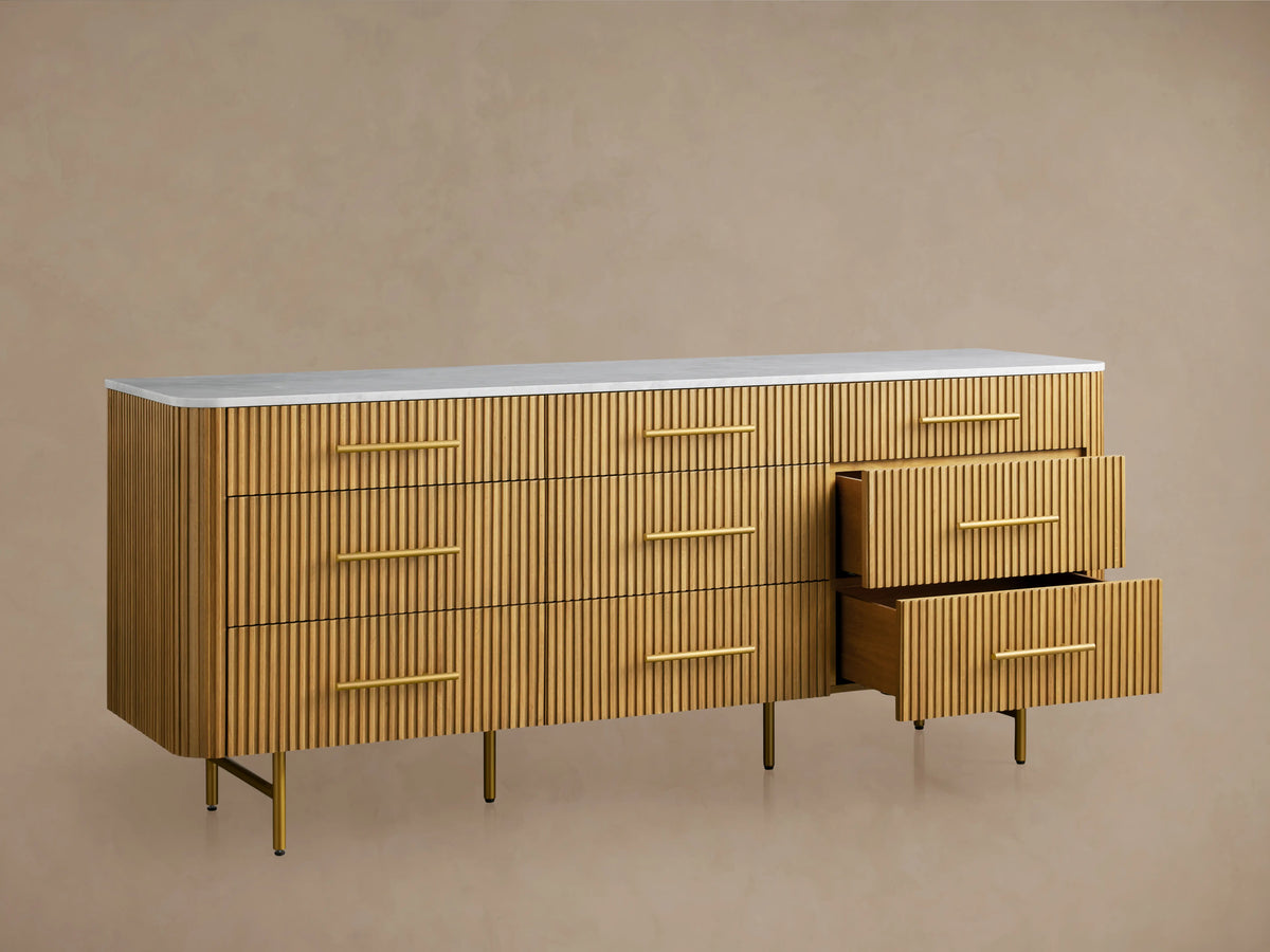 Finnley Nine-Drawer Dresser: light brown reeded wood with white marble top, gold bar handles, and angled gold legs.