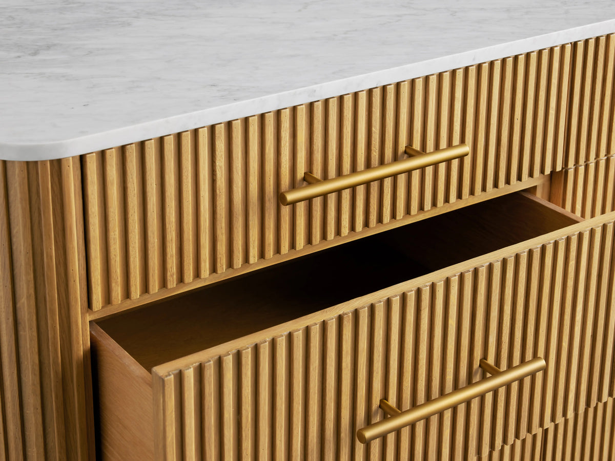 Finnley Nine-Drawer Dresser in honey wood with reeded front, white stone top, brass handles & legs. Two right drawers open.