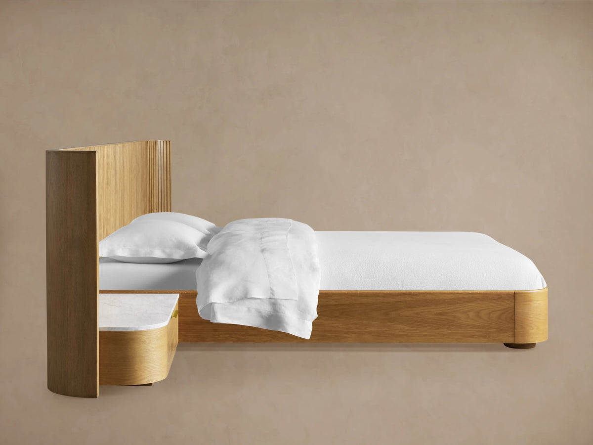 Finnley headboard detail: light wood with curved reeding, white marble top, and open drawer with brass handle.