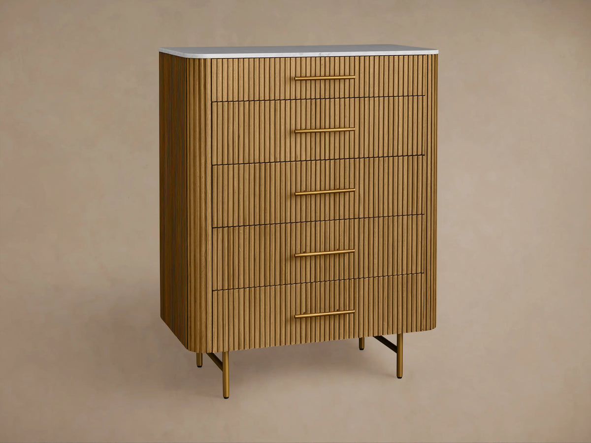Finnley Five-Drawer Dresser, light brown reeded wood, white stone top, brass handles & angled legs, front view.