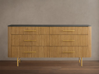 Finnley Six-Drawer Dresser, honey wood with vertical reeding detail, dark stone top, brass handles, on gold metal legs.