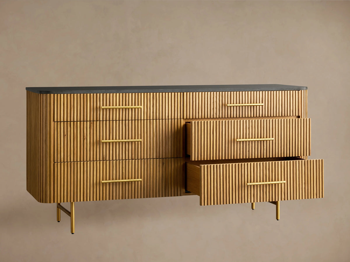 Finnley Six-Drawer Dresser, honey wood with vertical reeding detail, dark stone top, brass handles, on gold metal legs.