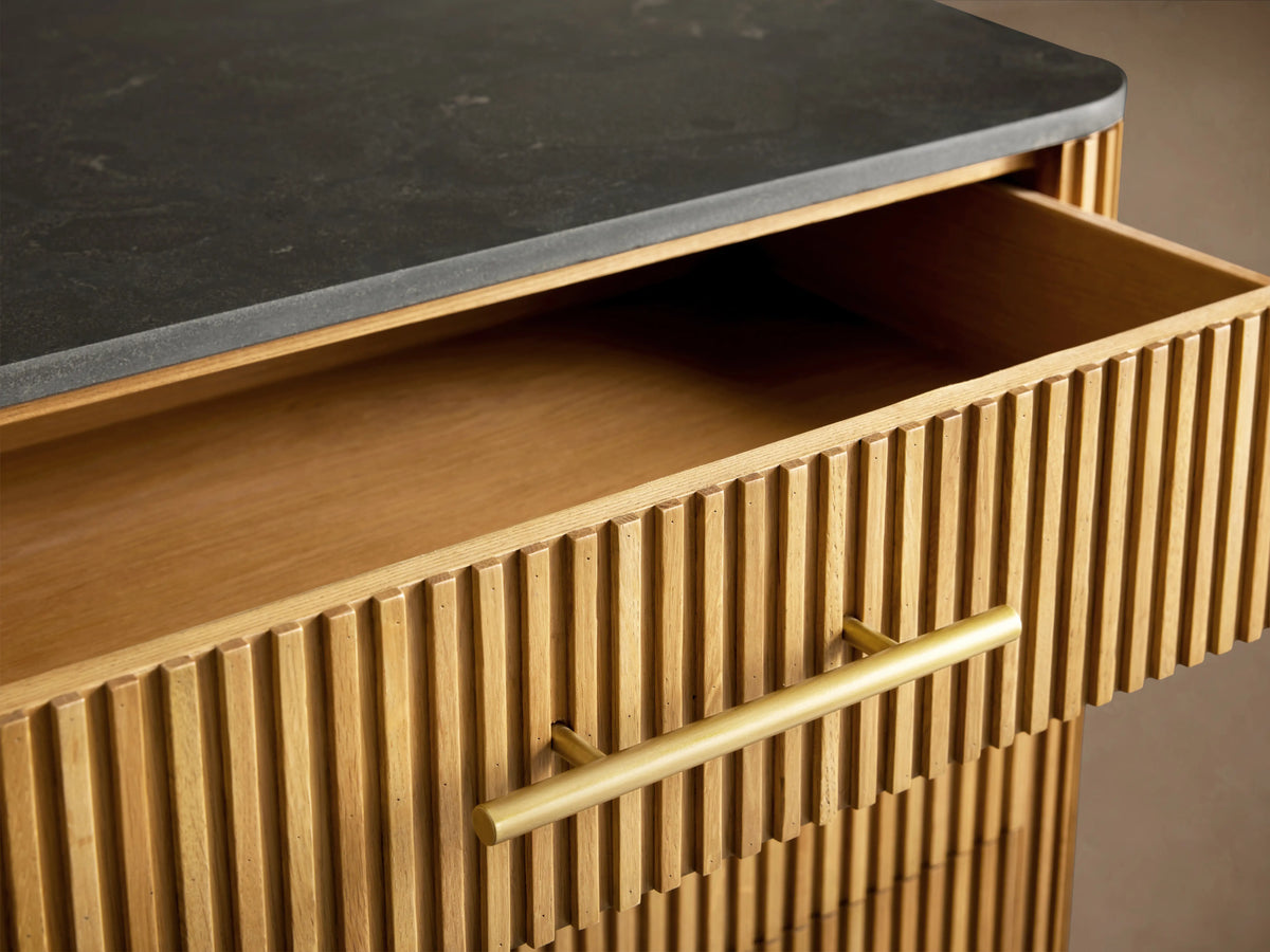 Finnley Six-Drawer Dresser with dark stone top, reeded light wood body, brass handles. Two right drawers partially open.