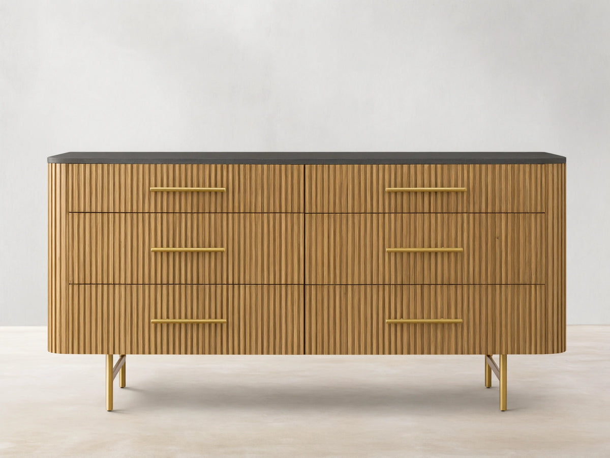 Finnley Six-Drawer Dresser, honey wood with vertical reeding detail, dark stone top, brass handles, on gold metal legs.