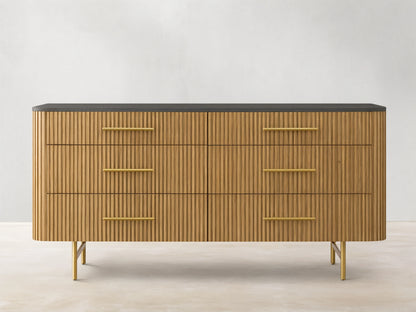 Finnley Six-Drawer Dresser, honey wood with vertical reeding detail, dark stone top, brass handles, on gold metal legs.