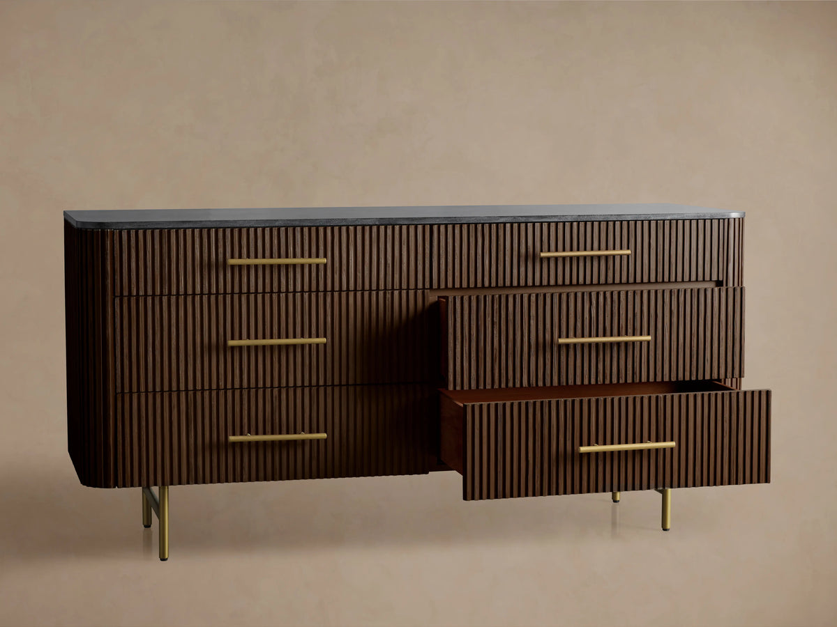 Finnley Six-Drawer Dresser in dark wood finish with vertical grooves, brass-finished handles, topped with a dark stone surface.