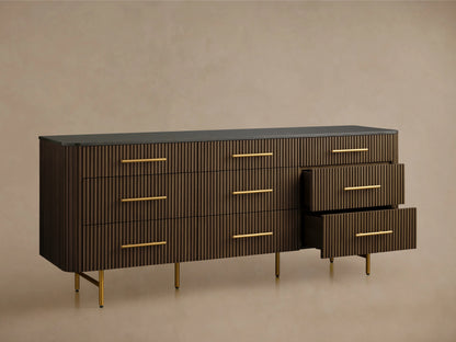 Finnley Nine-Drawer Dresser in dark wood finish with vertical grooves, brass handles, and slim brass legs, on a wooden floor.