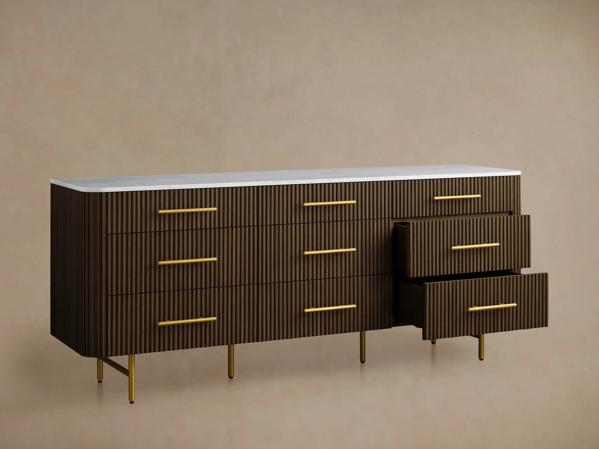 Finnley Nine-Drawer Dresser with a rich wood grain finish, brass handles, and a sleek white top, resting on brass legs.