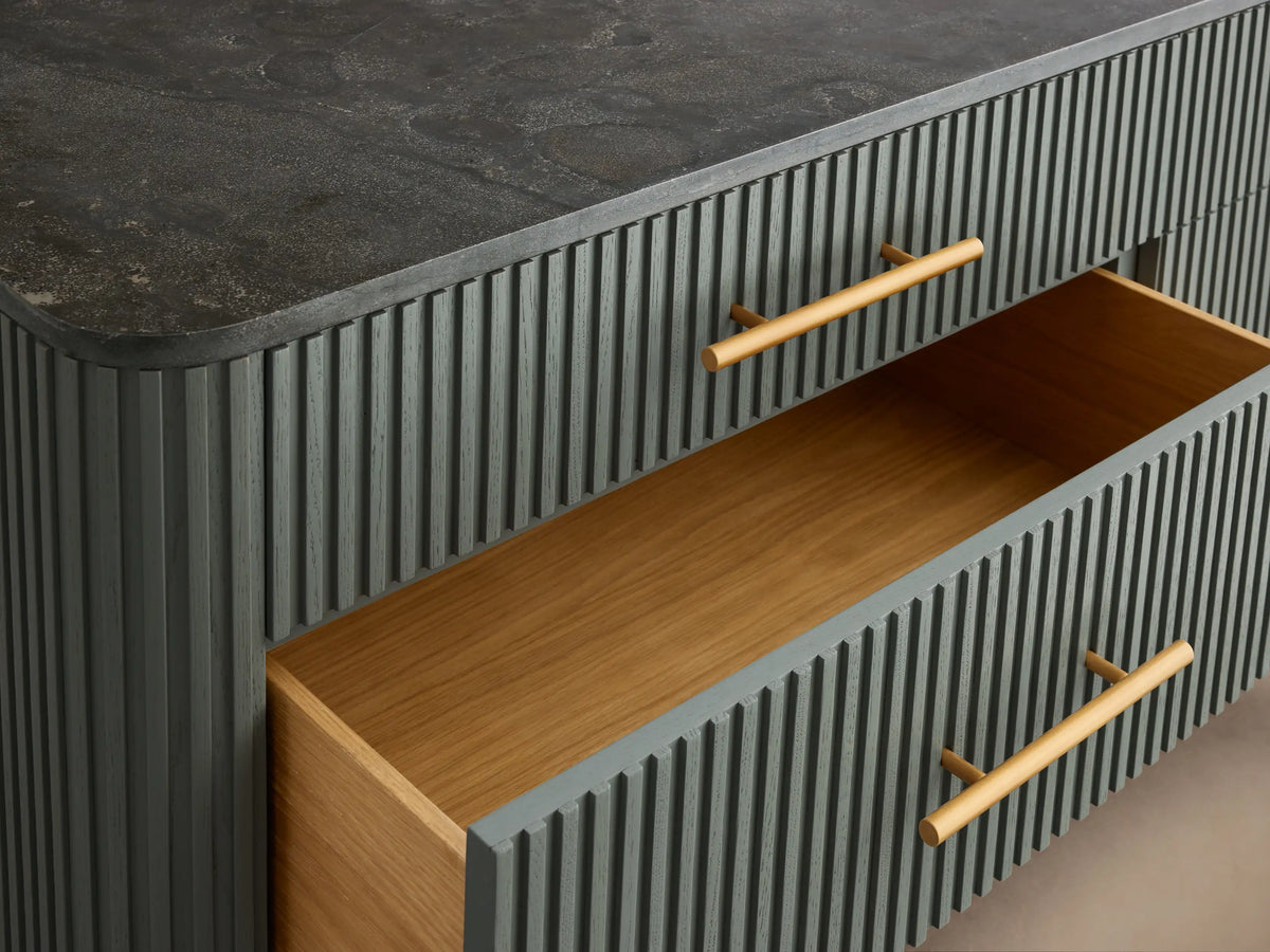 Finnley Six-Drawer Dresser in slate green with vertical reeding, dark stone top, brass bar handles, and angled brass legs.