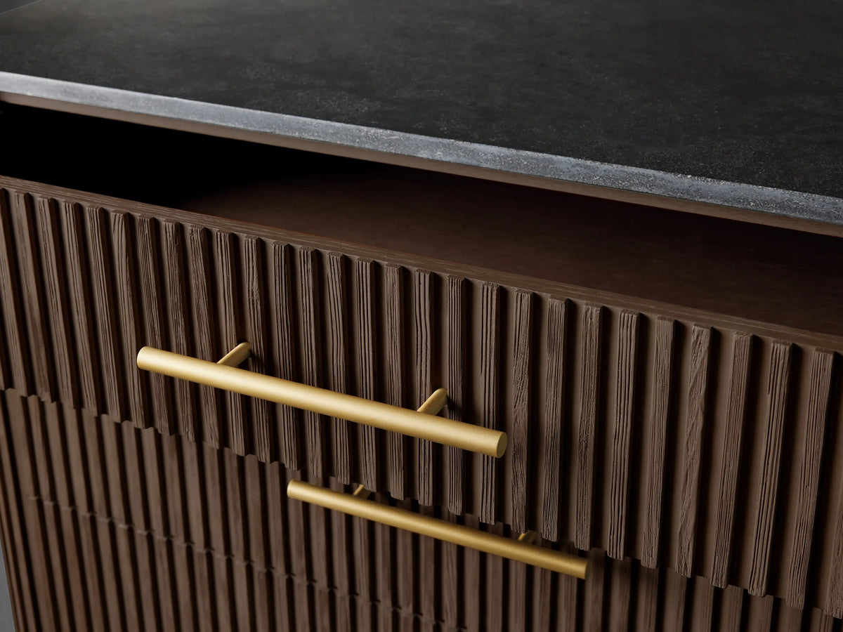 Close-up of Finnley Five-Drawer Dresser: dark brown reeded wood, two gold bar handles. Top drawer slightly open; black stone top.