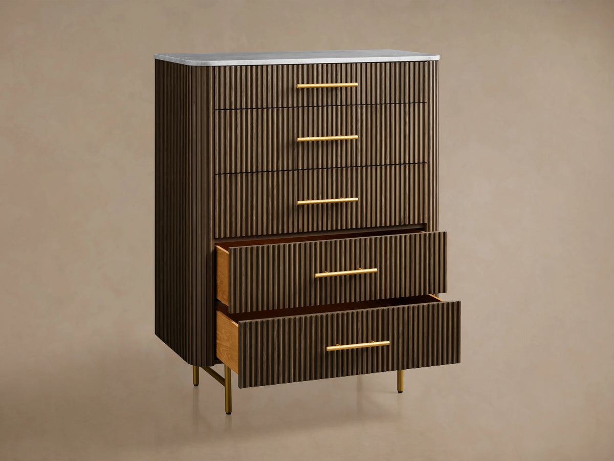 Finnley Five-Drawer Dresser with dark wood paneling, brass-finished handles, and a white marble top on a wooden floor.
