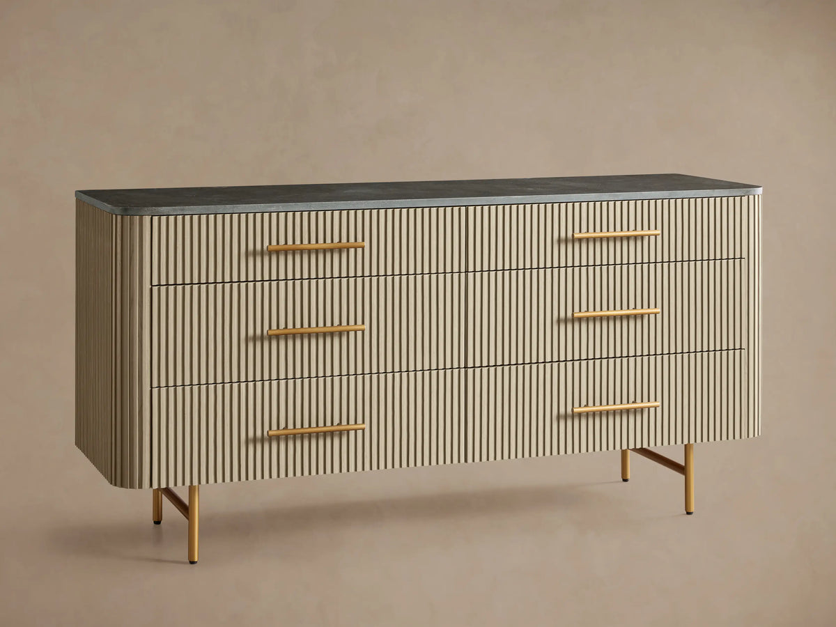 Finnley Six-Drawer Dresser with light reeded body, dark stone top, six drawers with brass handles, on angled brass legs.