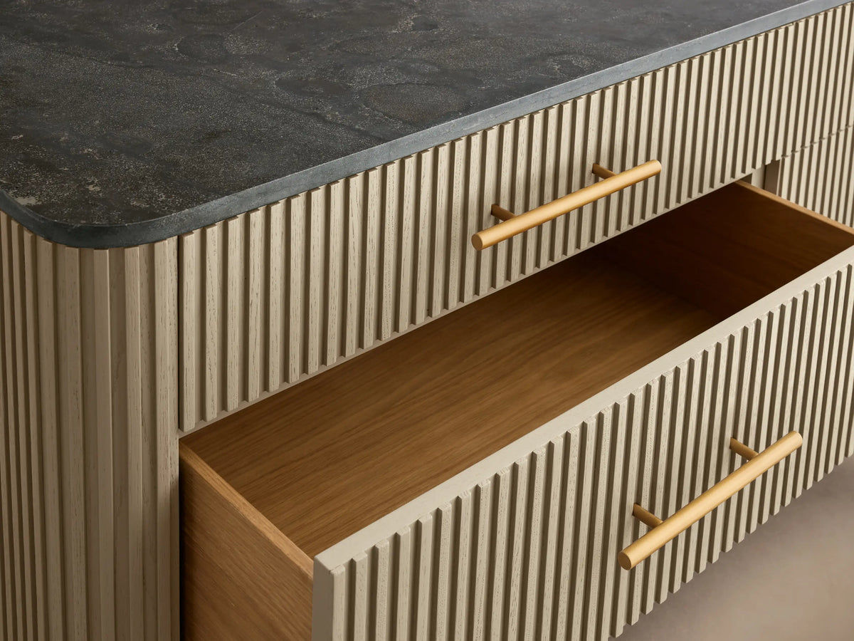 Finnley Six-Drawer Dresser with a light reeded body, dark stone top, six horizontal brass handles, and angled gold legs.
