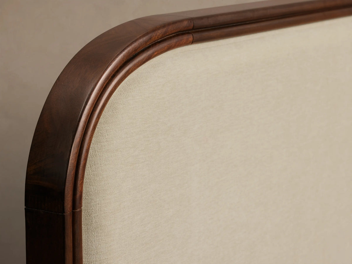 Close-up of the Frances Bed headboard, featuring a curved dark mahogany frame with carved detail and light cream upholstered fabric.