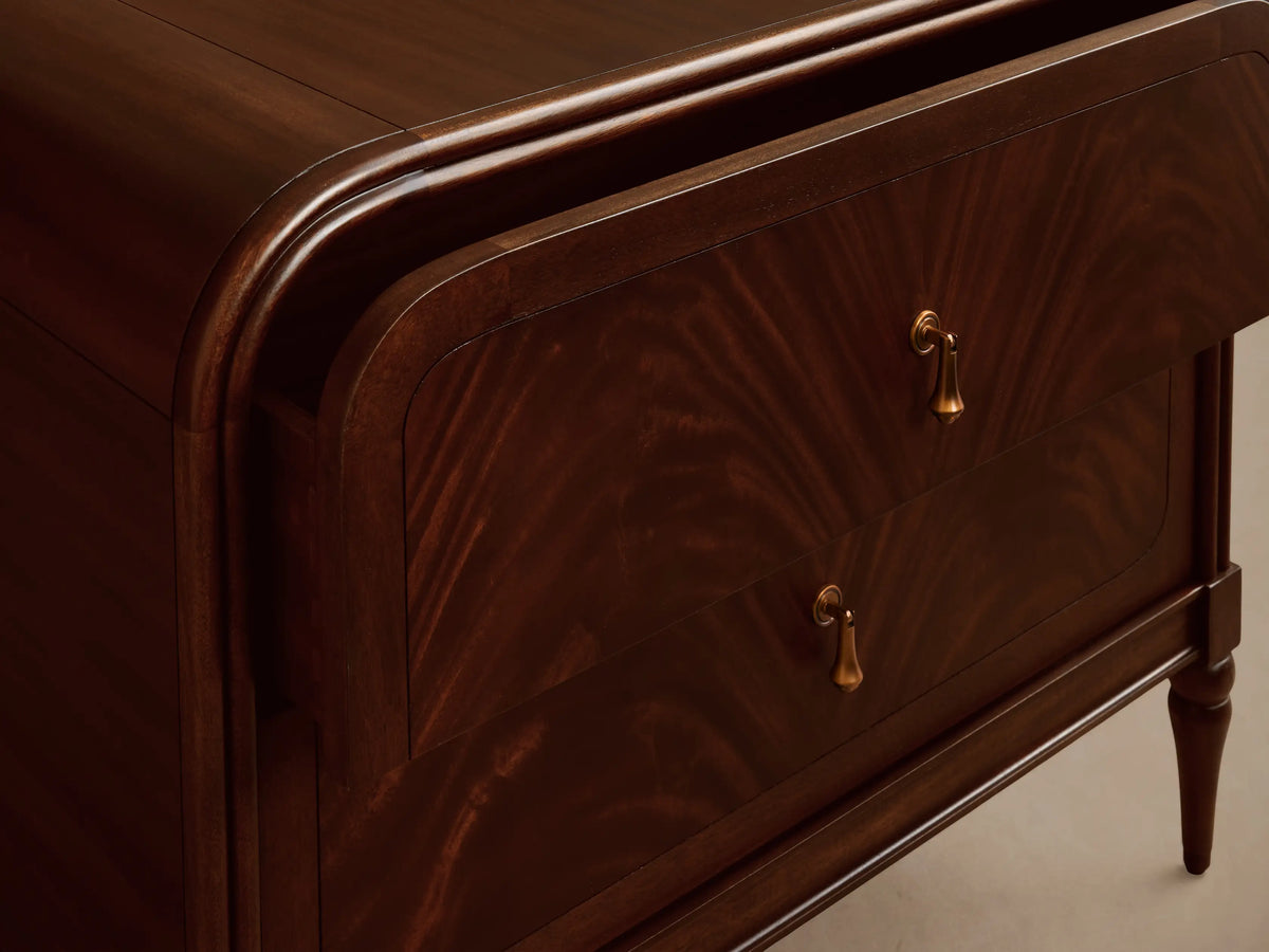 Frances Nightstand, dark mahogany wood with flame-like grain. It has two drawers with vintage brass pulls, rounded top, and tapered legs.
