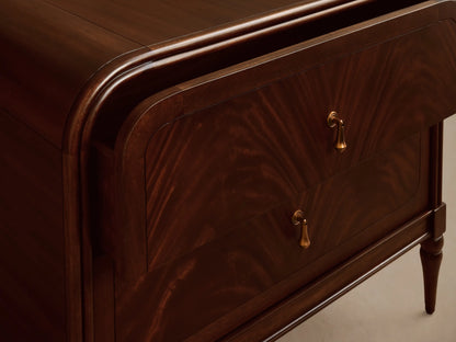 Frances Nightstand, dark mahogany wood with flame-like grain. It has two drawers with vintage brass pulls, rounded top, and tapered legs.