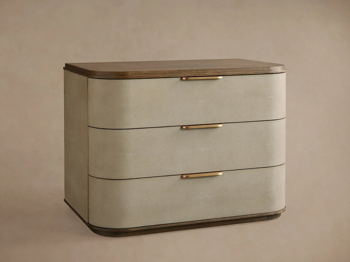 Charbon faux shagreen Harrow Nightstand with three bronze-handled drawers, next to a bed.
