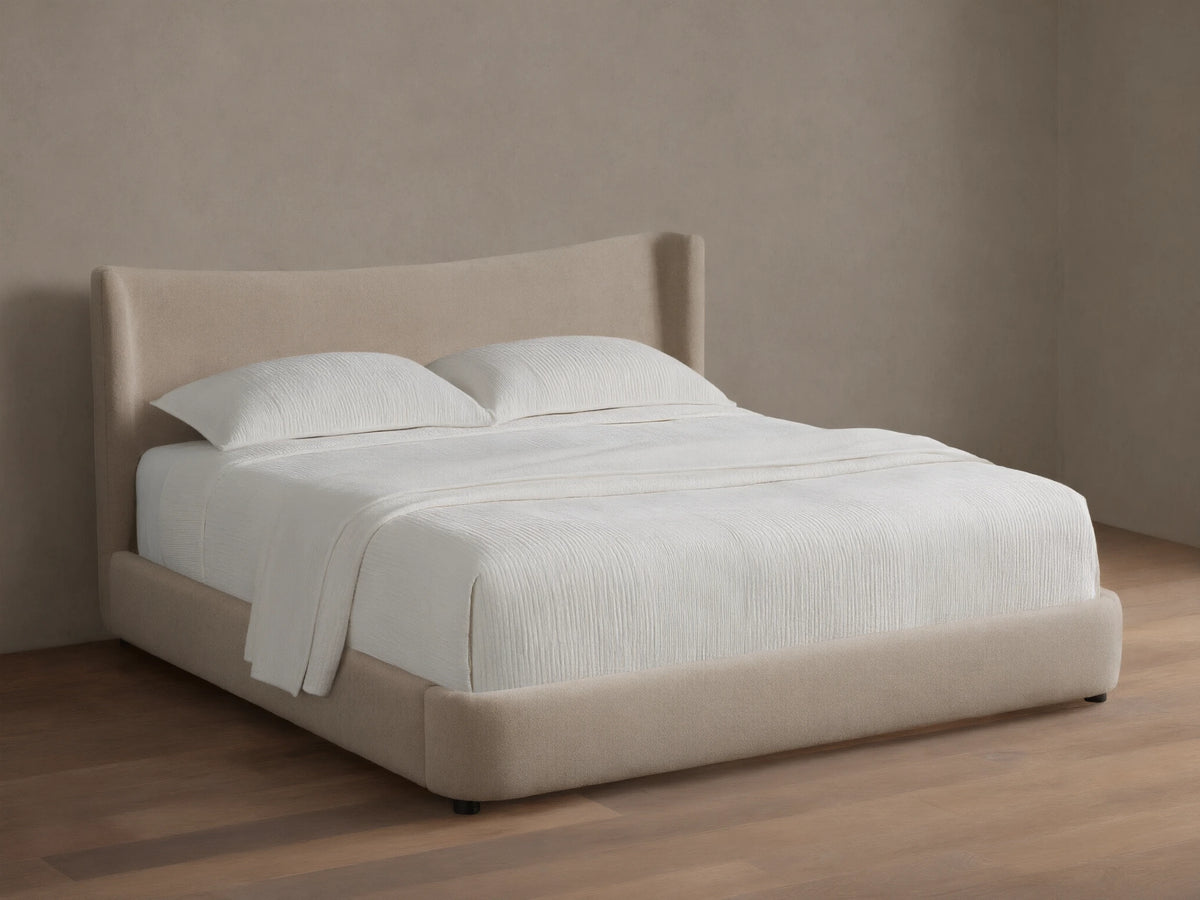 Front view of the beige upholstered Hathaway Bed, showing its curved headboard and platform, with off-white ribbed bedding.
