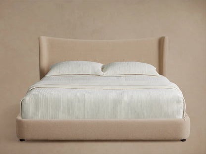 Front view of the beige upholstered Hathaway Bed, showing its curved headboard and platform, with off-white ribbed bedding.