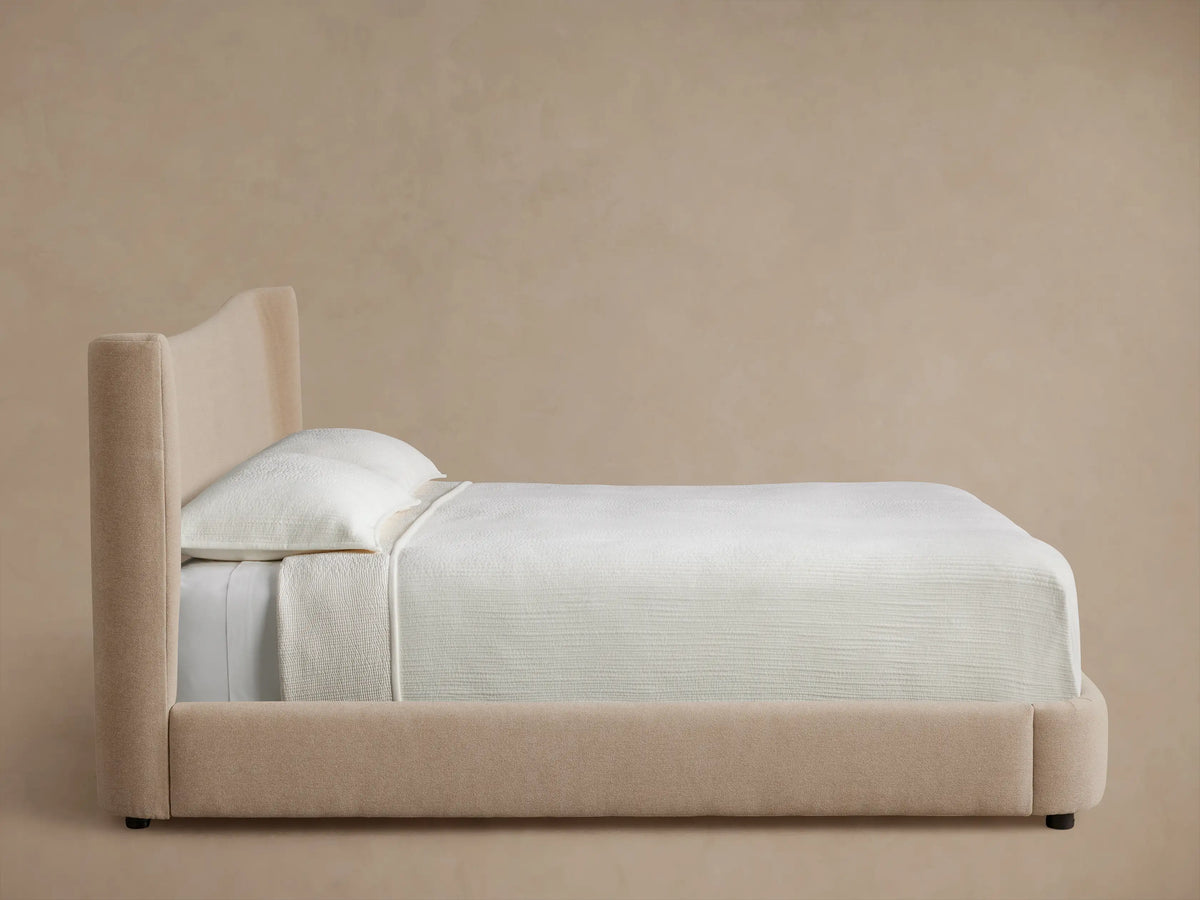 Front view of a beige upholstered Hathaway Bed with a tall, slightly curved headboard, made up with white bedding.