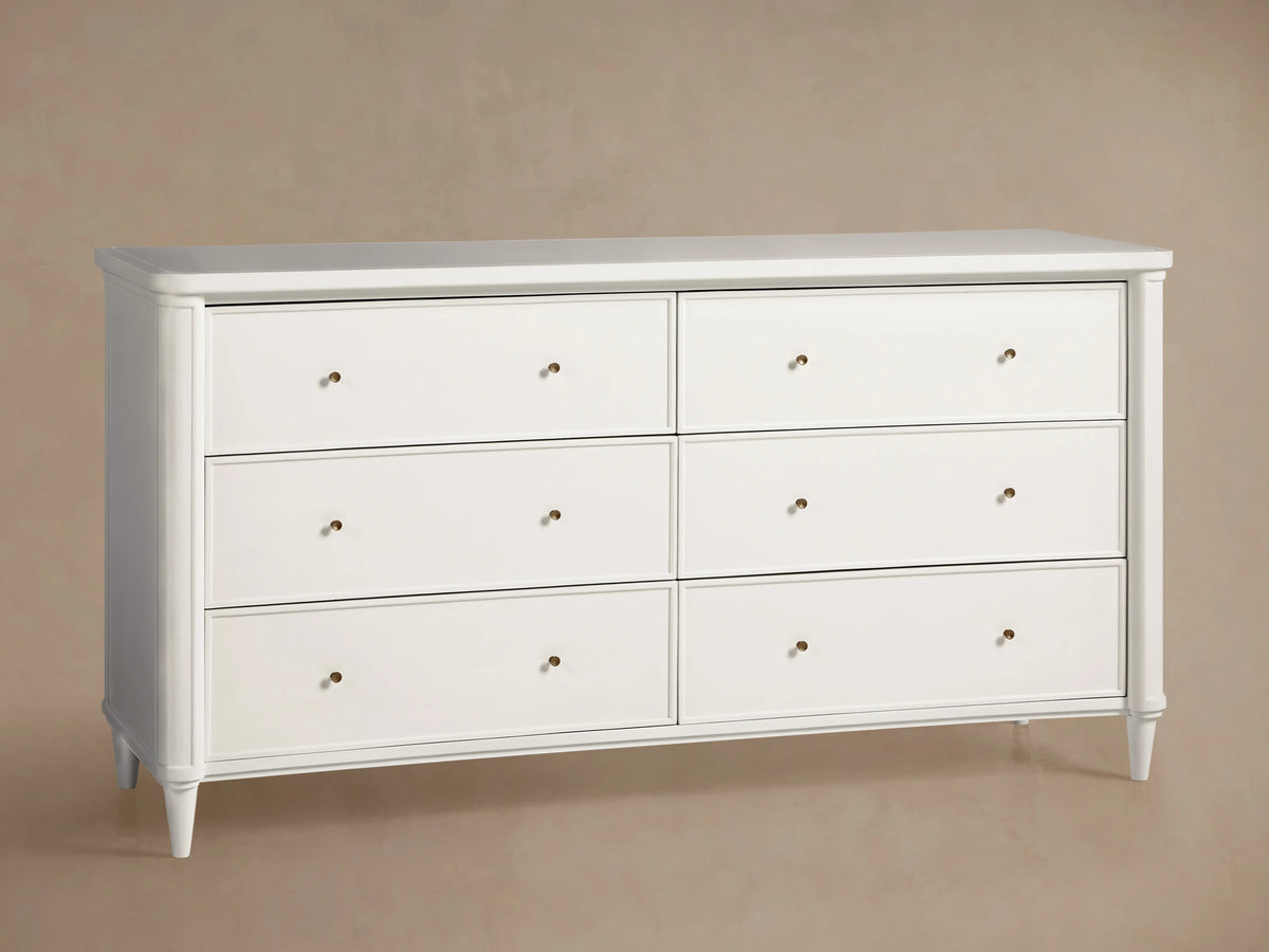 Front view of dark gray Henley Wide Six-Drawer Dresser with brass pulls, a lamp, and vase of flowers in a bedroom.