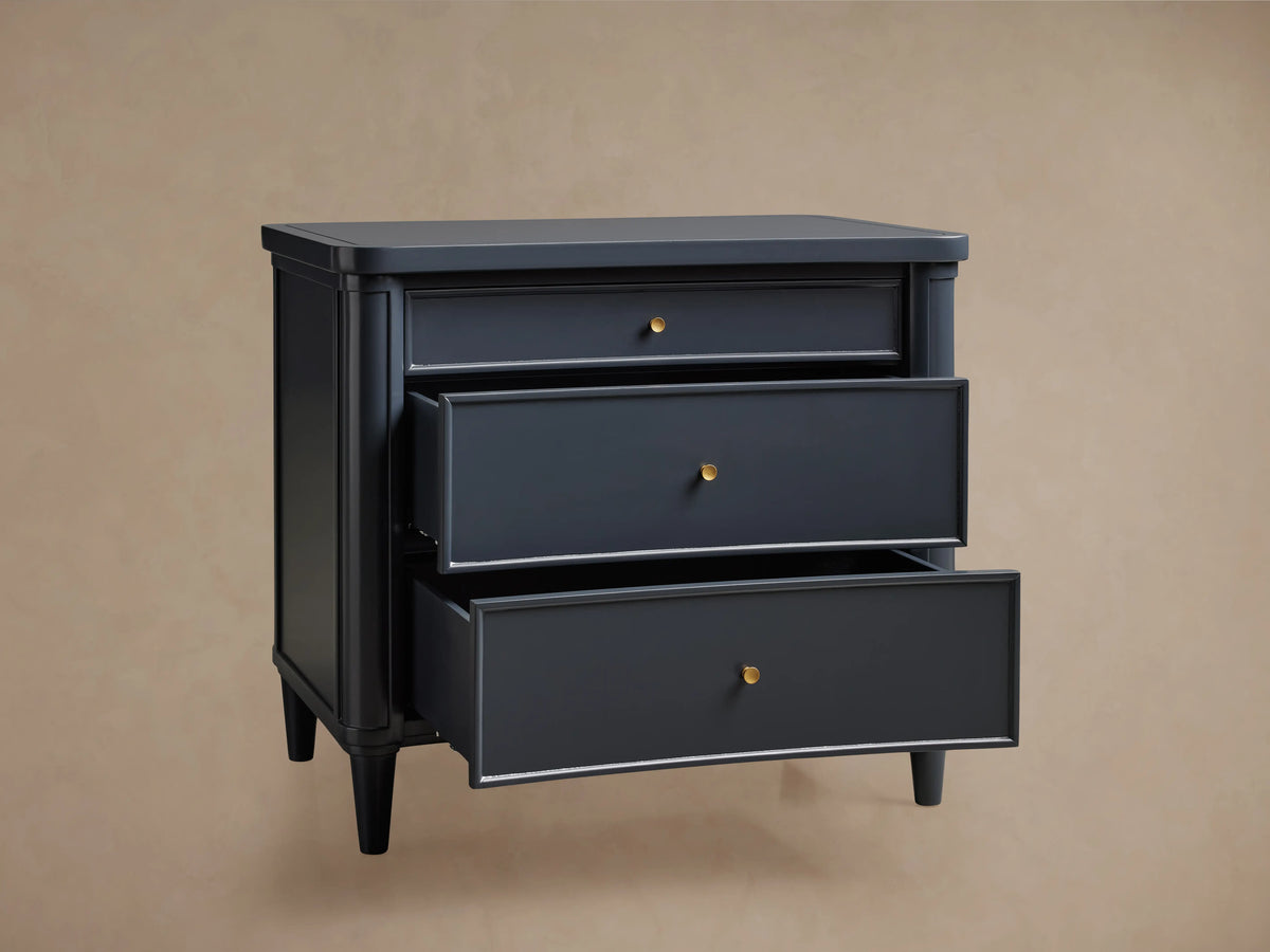 Henley Nightstand, dark blue, with three paneled drawers, brass pulls, and tapered legs. Front view on wood floor.