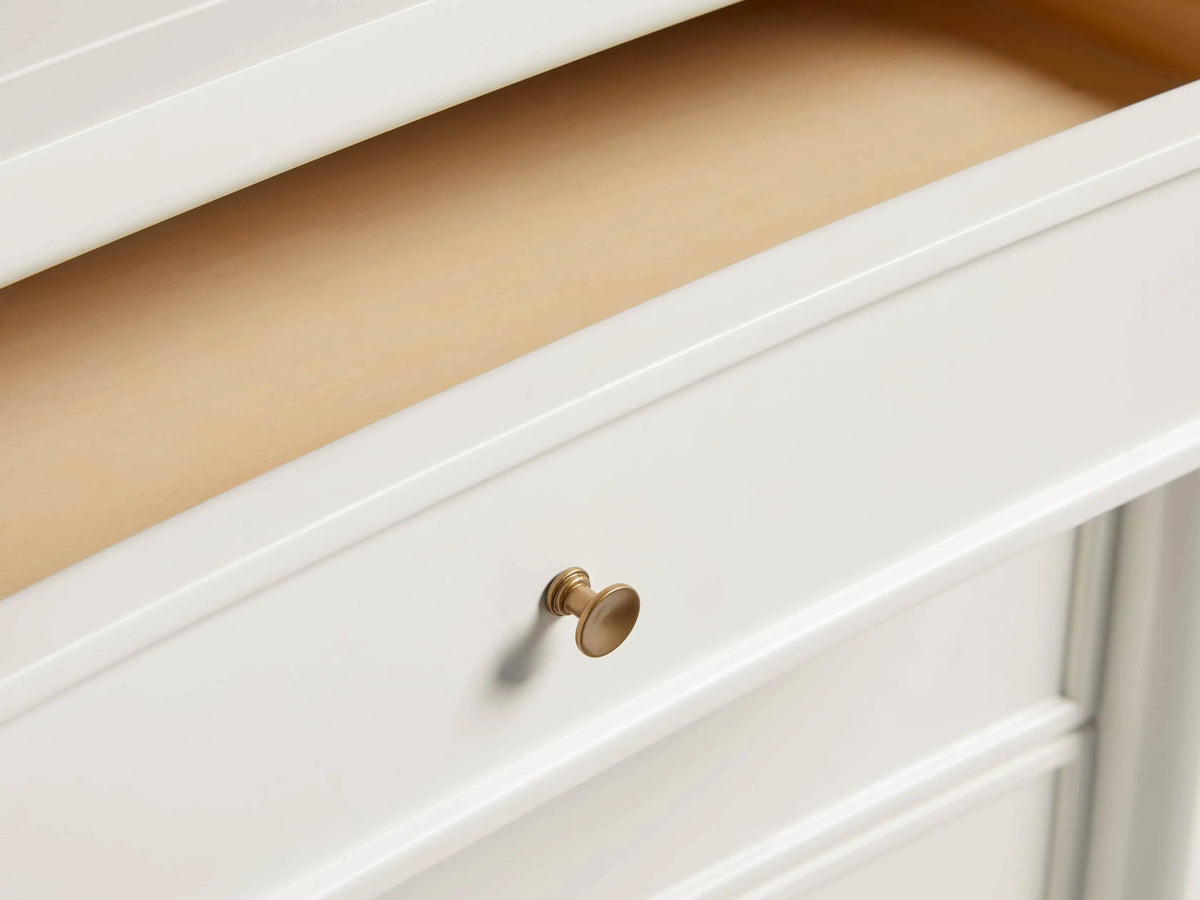 Henley Nightstand in white finish with three drawers, petite brass pulls, and tapered legs, set against a wooden floor.