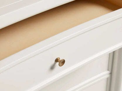 Henley Nightstand in white finish with three drawers, petite brass pulls, and tapered legs, set against a wooden floor.