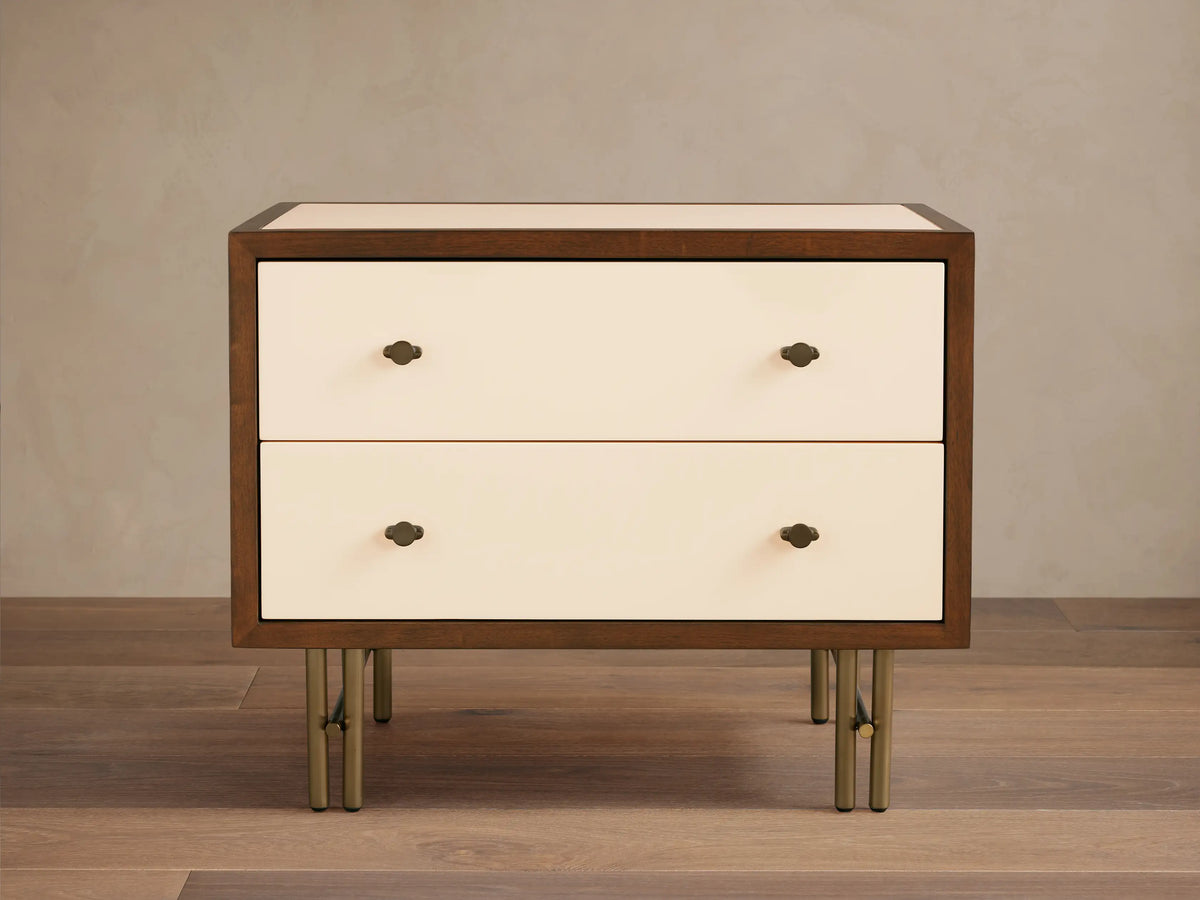 Henton Nightstand: dark wood frame, two cream high-gloss drawers with brass knobs, and sleek brass metal legs on wood floor.