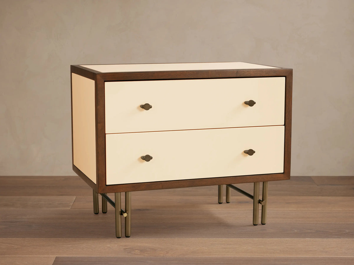 Henton Nightstand: dark wood frame, two cream high-gloss drawers with brass knobs, and sleek brass metal legs on wood floor.