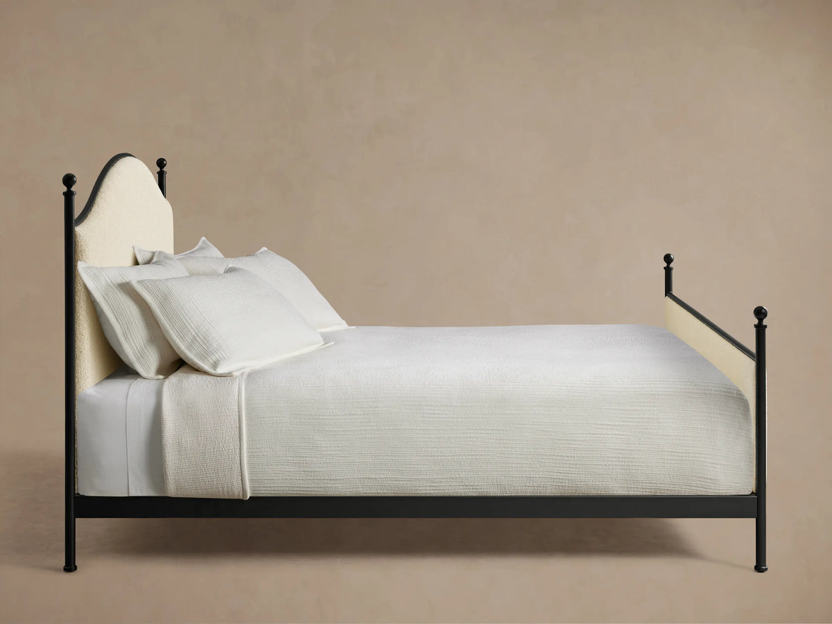 Front view of the Kimber Upholstered Bed with cream upholstered panels, matte black iron frame, and finial details. White bedding.