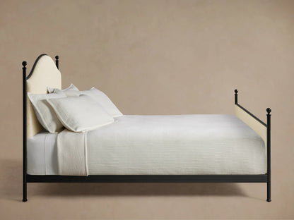 Front view of the Kimber Upholstered Bed with cream upholstered panels, matte black iron frame, and finial details. White bedding.