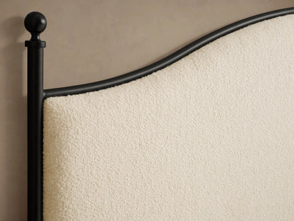 Side view of the Kimber Upholstered Bed with matte black iron frame, finial details, cream upholstered panels, and white bedding.