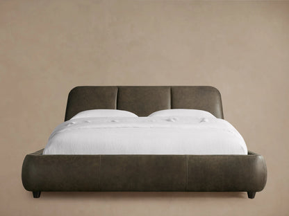 Front view of the dark brown Kinnan Leather Bed with a rounded, three-paneled headboard, upholstered frame, and white bedding.