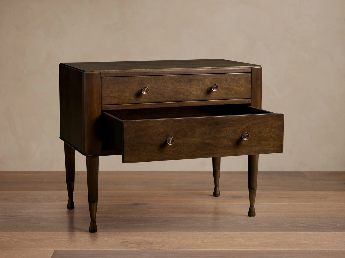 Laurent Nightstand with two visible drawers, one open, crafted in dark mahogany wood, accented with patinaed brass feet, on wood floor.