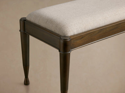 Laurent Bench with a beige cushioned seat, dark mahogany wood frame, and patinaed brass-capped legs against a neutral background.